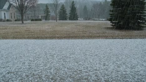 a large amount of hail falling from the sky and piling up on a driveway in a rural neighborhood