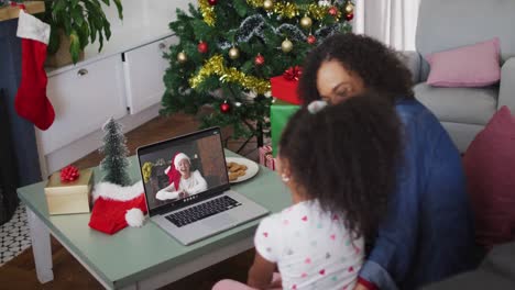 Happy-african-american-mother-and-daughter-on-video-call-with-female-friend-at-christmas-time