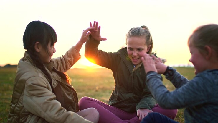 Tre bambine che giocano al gioco delle mani battute all'aperto al tramonto