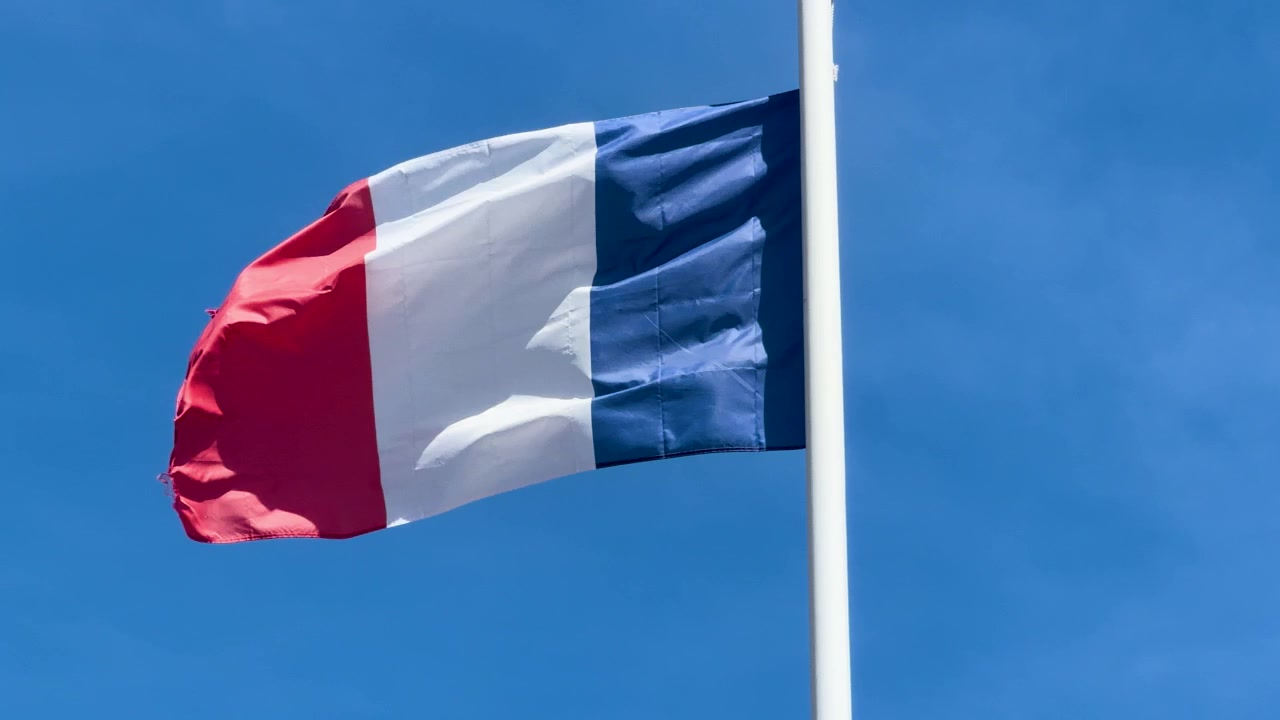 La bandiera nazionale della Francia sventola stabilmente su un'asta bianca sotto un cielo azzurro e limpido.