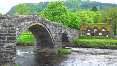 un hermoso puente sobre un río con una casa cubierta de musgo en la distancia gales