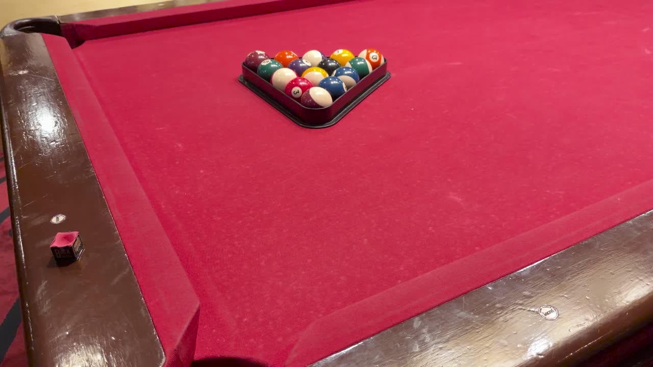 Cue ball hits racked billiard balls on red table in elegant, warmly lit bar interior
