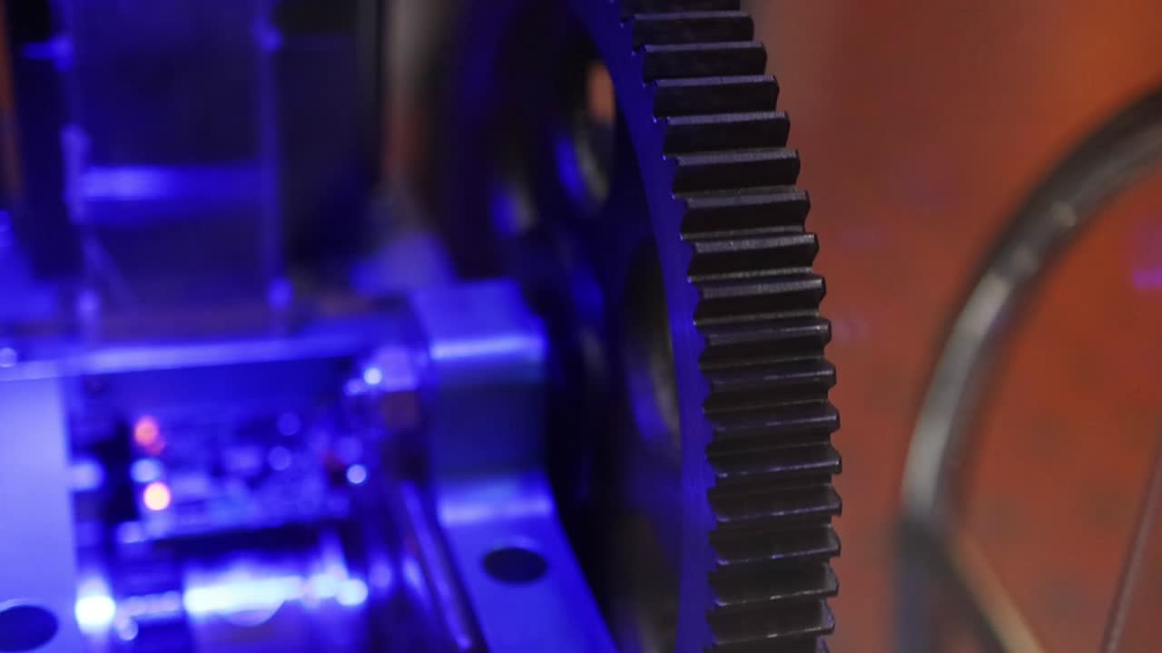 Detailed view of mechanical gear teeth rotating within an industrial exhibit under blue light