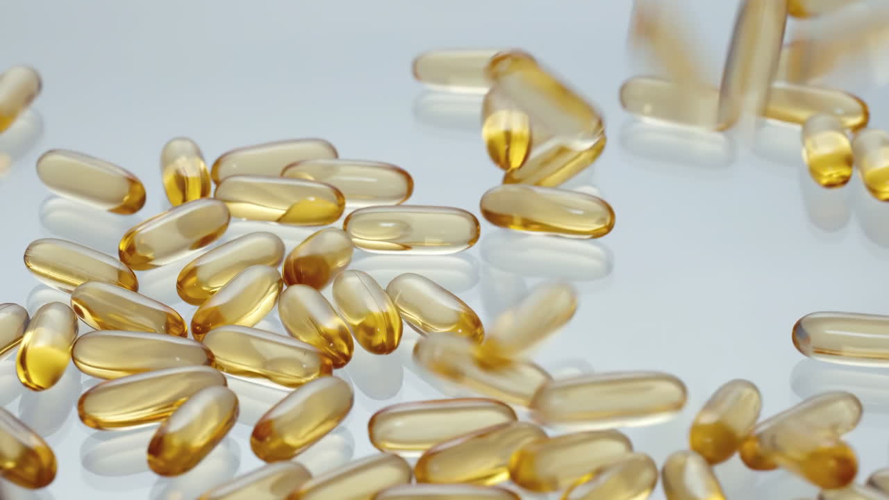 Capsule di integratori farmaceutici dorati in caduta, pillole in softgel di olio di vitamina D o omega-3 che cadono e rimbalzano su una superficie riflettente, integratori alimentari per una vita sana, medicina, farmacia, salute.