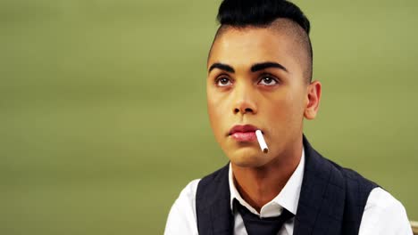 androgynous man posing with cigarette against green background