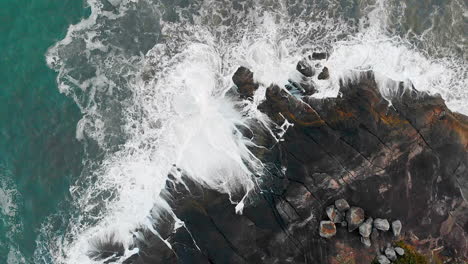 aerial view waves break on rocks