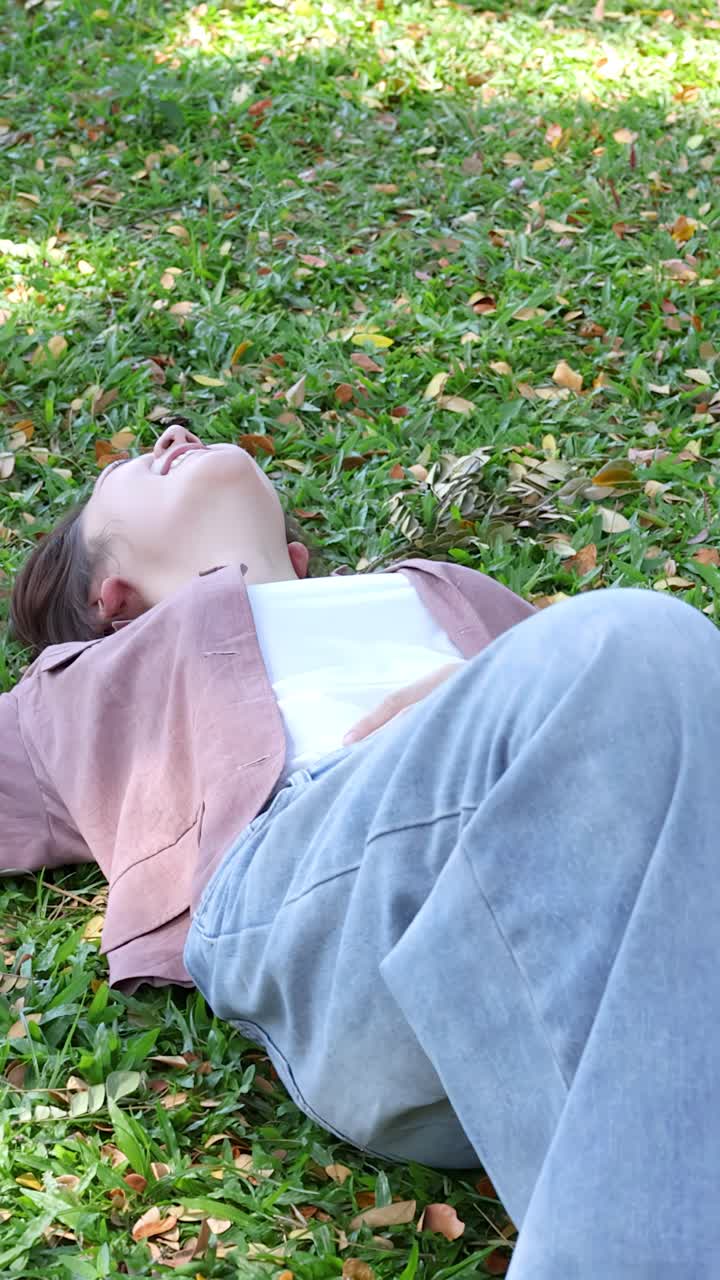 Uno studente universitario thailandese sorridente è sdraiato sull'erba verde prima di alzarsi a sedere sotto il sole splendente.