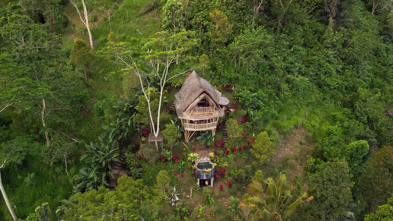 Drone footage showcasing a handcrafted bamboo eco house hidden in the green hills of Sidemen Bali. The scene highlights lush forest vegetation, natural design, and peaceful tropical living