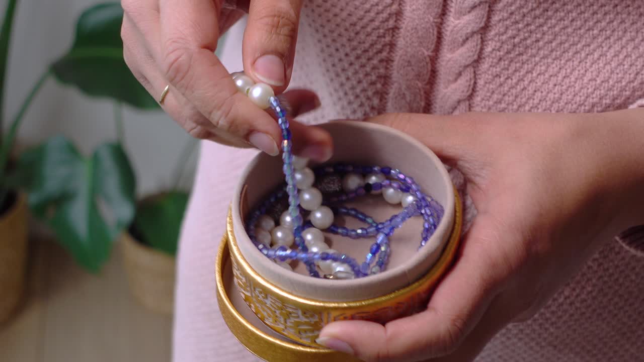 Mani che selezionano gioielli di perle e perline da una piccola scatola