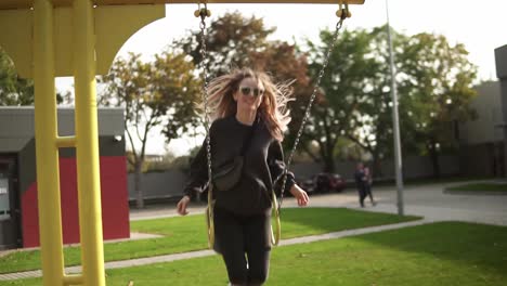 long haired woman swinging on a swing in the green park, happily smiling