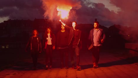 group of happy teenagers with one holding and waving signal flare walking forward towards camera at night.