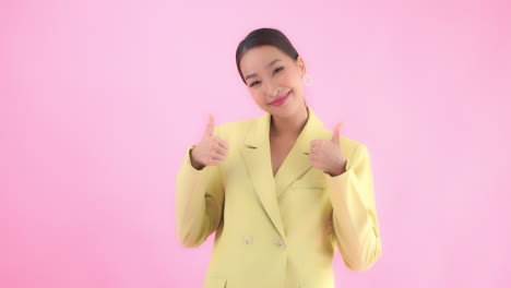 medium close of a young businesswoman in a business appropriate suit raises her hands into view giving the thumbs up to the viewer