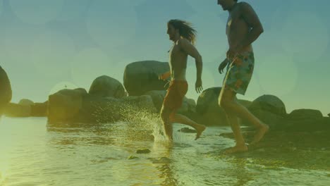 Animation-of-glowing-lights-over-group-of-male-friends-running-to-the-sea