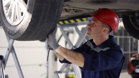 Auto-mechanic-working-underneath-car-lifting-machine-at-the-garage