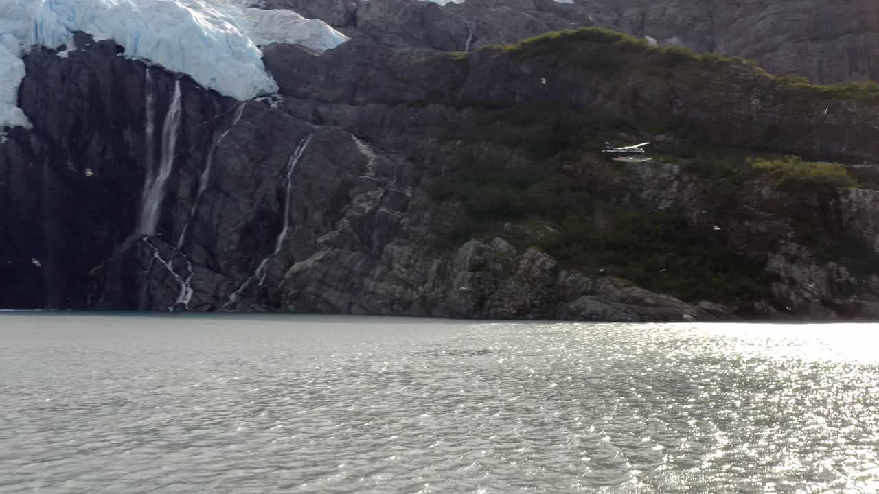 미국 알래스카에서 일출 동안 졸졸 흐르는 바닷물로 눈산을 통과하는 경비행기