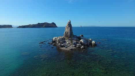 hovering aerial of small rock island and birds flying around it with background islands