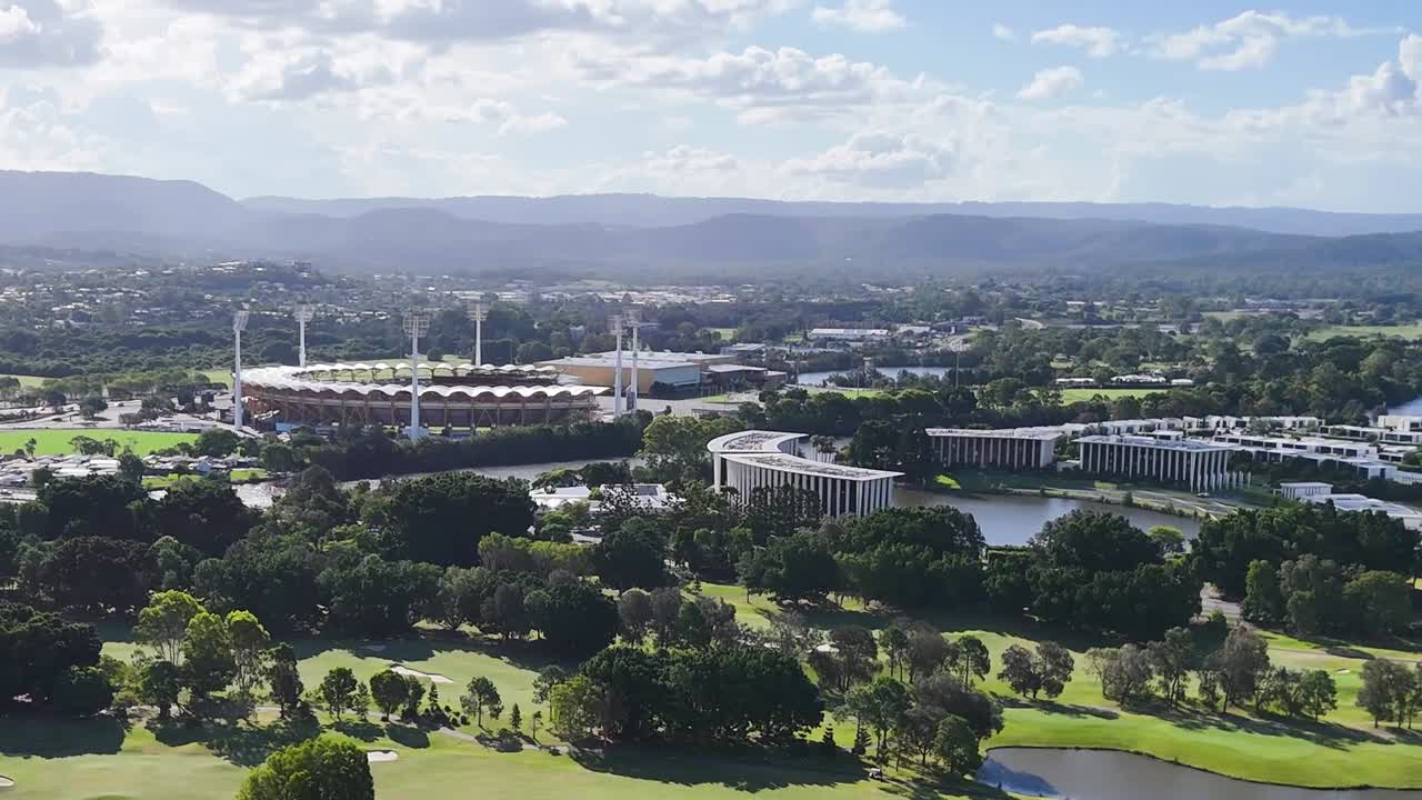 High-definition aerial view showcasing a golf course, river, and urban buildings under a bright sky.