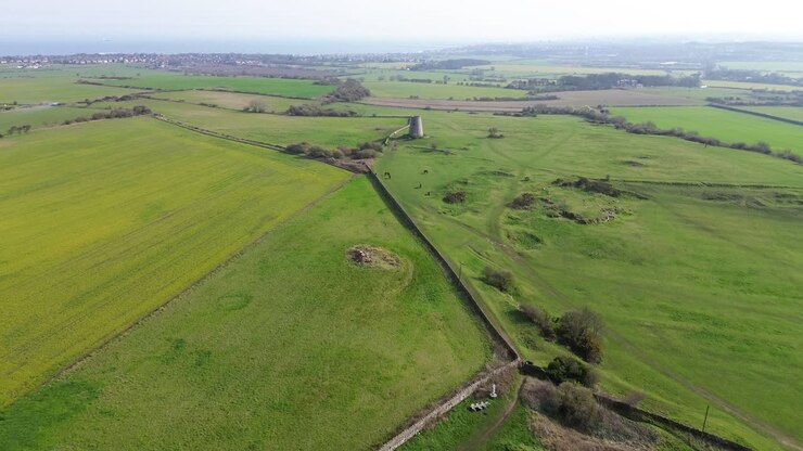 Cleadon Windmill drone flight away across open green farmland and rolling fields in Cleadon, South Tyneside, England, revealing rural landscape, paths and hedgerows