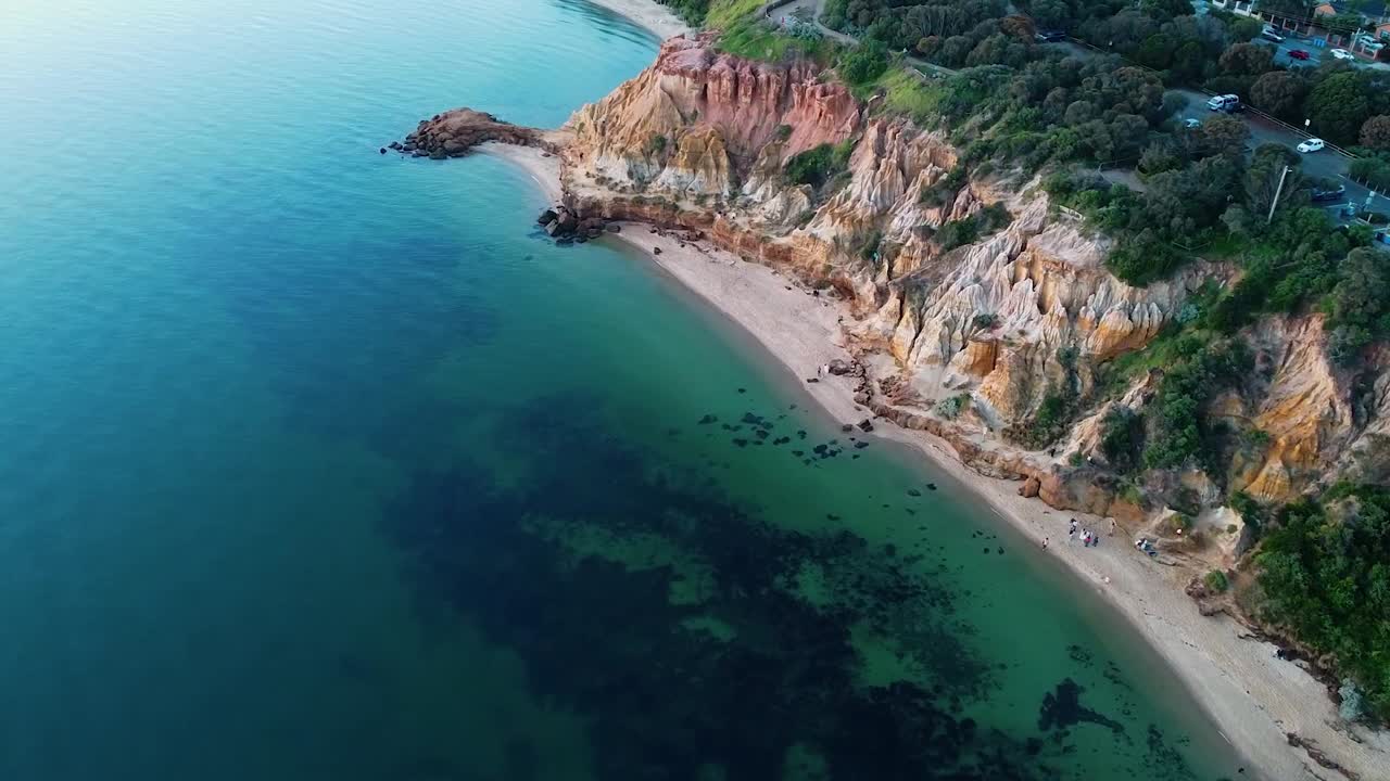 A dramatic drone shot of the Red Bluff cliffs, capturing their rugged beauty and vibrant colors against the vast ocean backdrop.