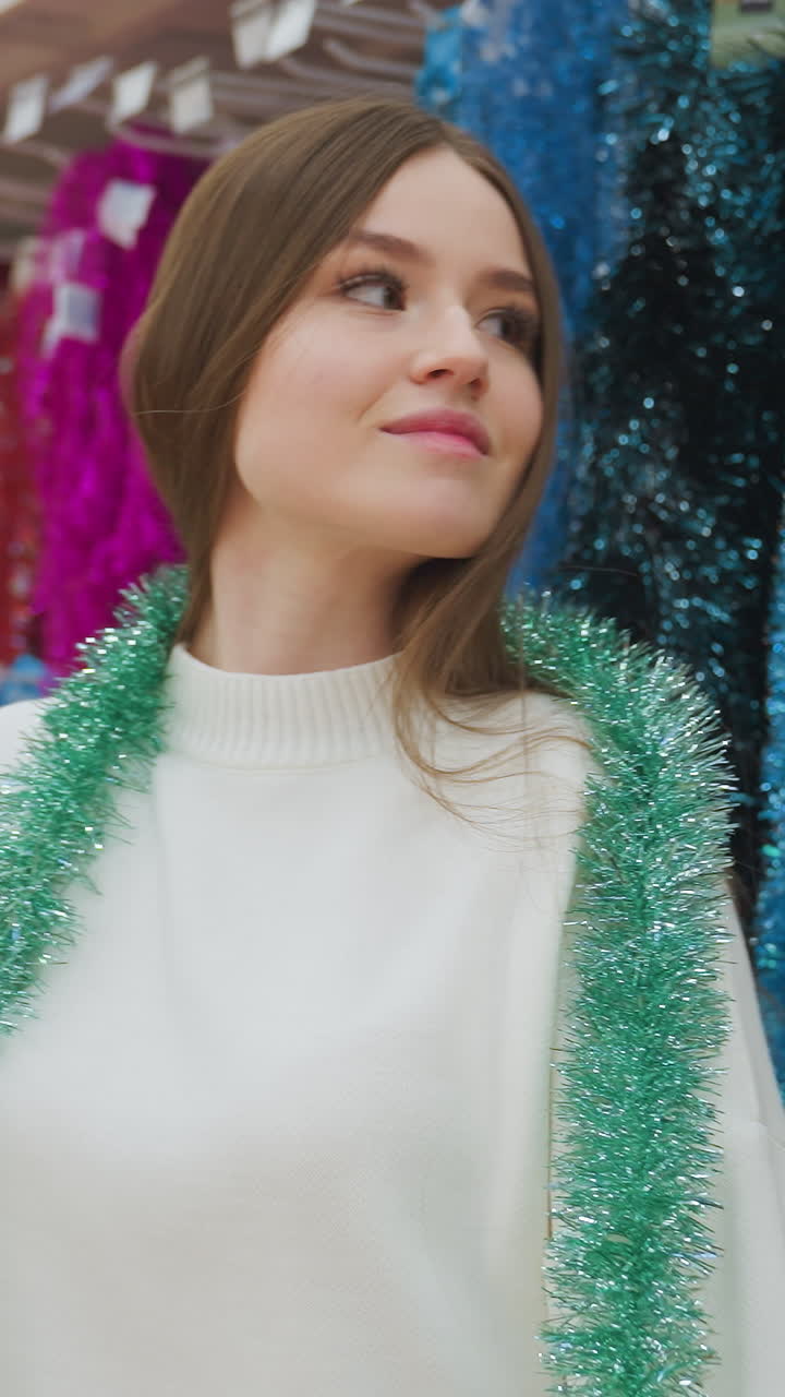 Lady smiles while checking out a shiny green Christmas decoration in decor store, she gently holds and observes the vibrant, festive decoration in the retail environment surrounded by colorful tinsel