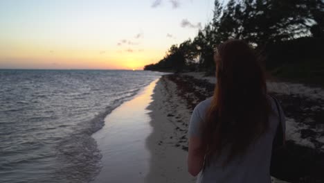 red headed woman taking a photo on her iphone on a tropical beach
