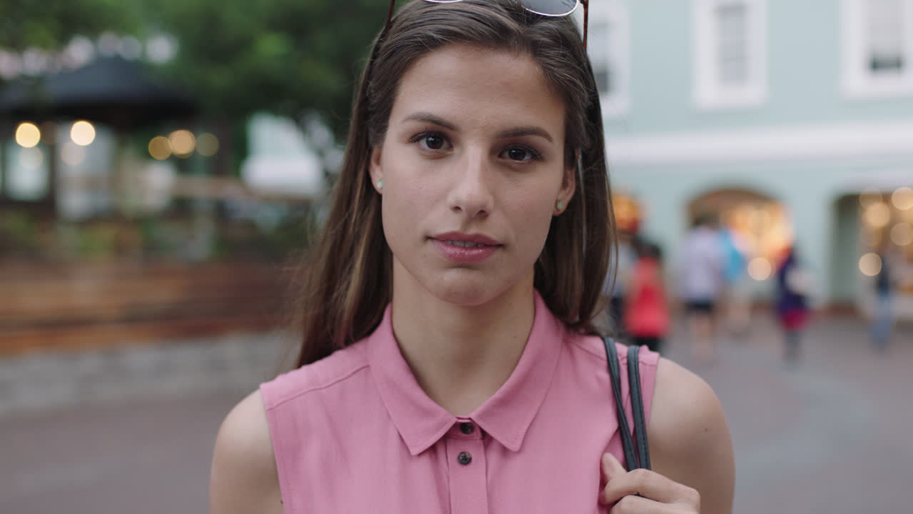 slow motion portrait of young beautiful woman wearing pink blouse smiling at camera looking pensive thoughtful evening urban background
