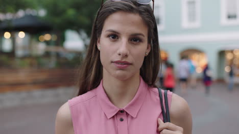 retrato en cámara lenta de una mujer joven y hermosa con una blusa rosa sonriendo a la cámara mirando pensativo reflexivo de la noche de fondo urbano