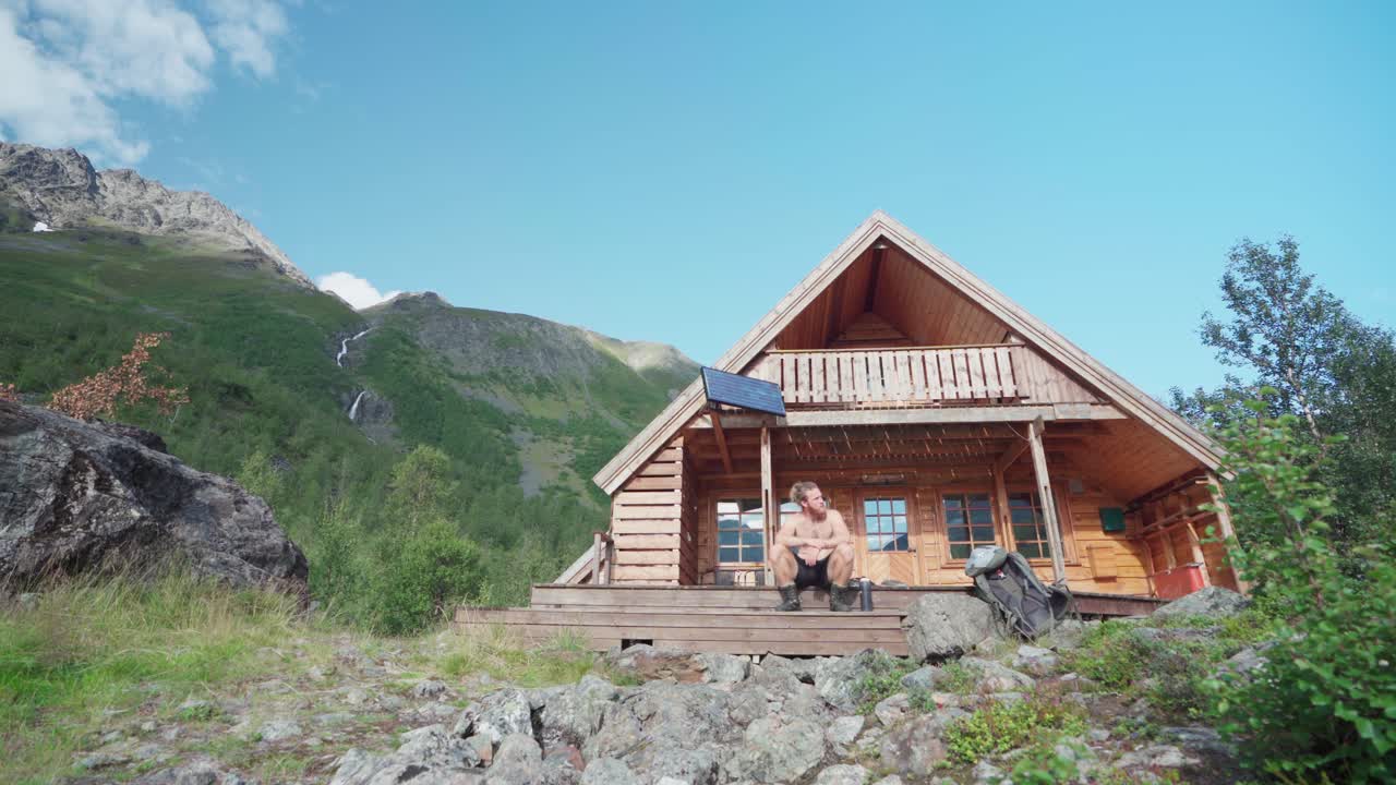 turista sin camisa relajándose sentado en los escalones del porche delantero de una cabaña de madera en el valle de lyngsdalen, noruega