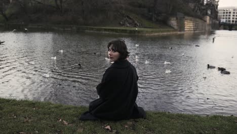 young woman in a black coat sitting in a park in autumn in afternoon and feeding ducks in a sea-4