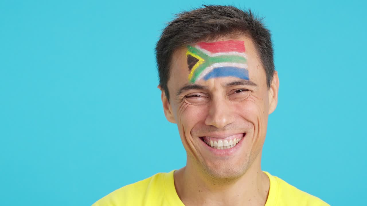 Man with a south african flag painted on the face smiling