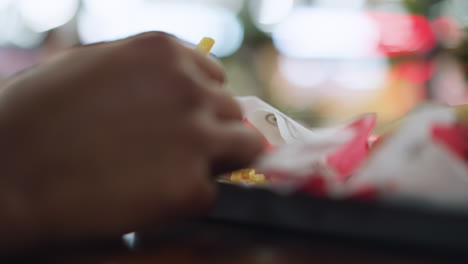 Unclear view of hand moving on tray on table, motion suggesting interaction with food or object, shallow depth of field creating soft shapes, casual indoor setting with ambient light