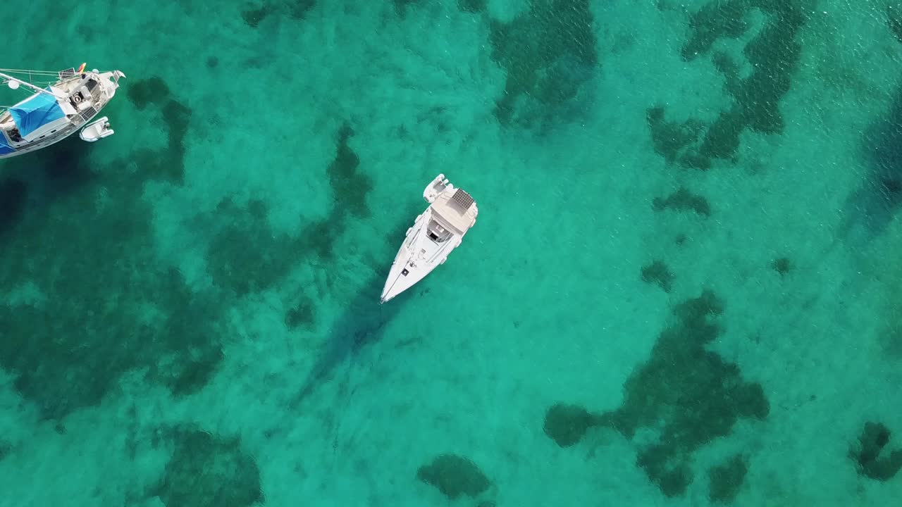 Greece,Samos Island's Posidonio Bay,Drone Footage starts from a sail boat anchored on the turquoise waters, zooms out slowly with a straight angle, at the end more boats and their shades are visible.