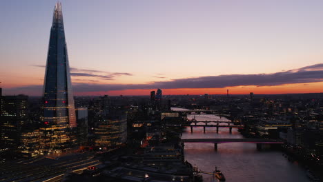 Evening-aerial-panoramic-view-of-Thames-river-flowing-through-city.-Shard-skyscraper-and-bridges-across-river-against-twilight-sky.-London,-UK