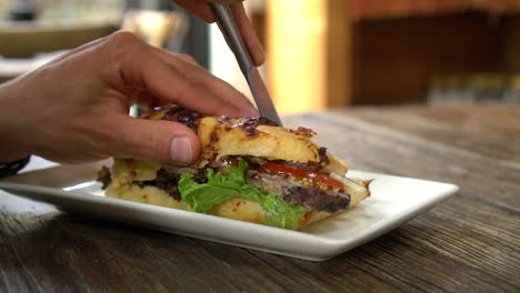 Slowmo---Kaukasischer-Mann-Schneidet-Rindfleischsandwich-Zum-Frühstück-Im-Stilvollen-Café