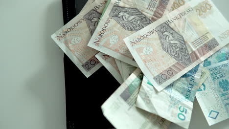 revelando billetes de efectivo arrugados en zloty polaco encima de una cartera de cuero negro