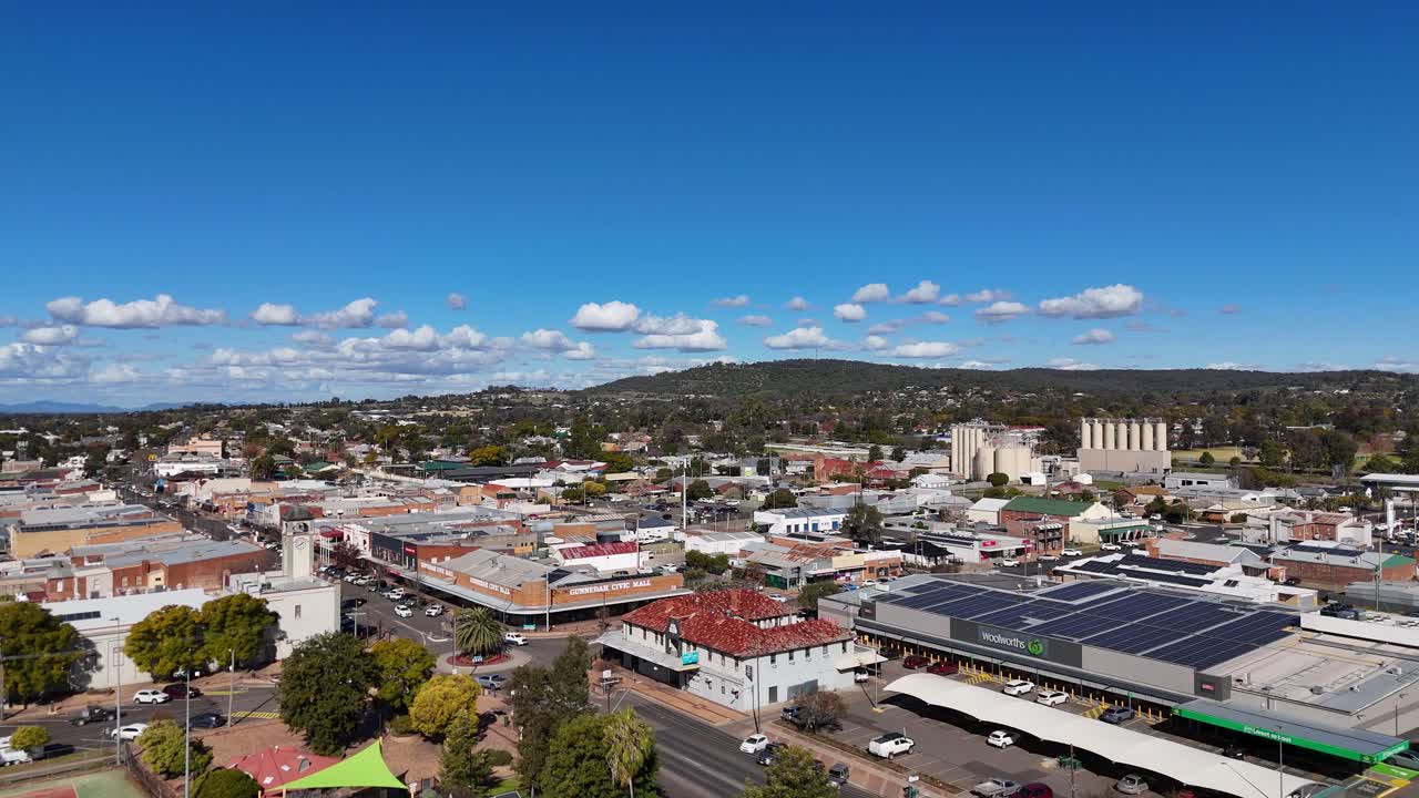 Drone camera smoothly pans above Glen Innes, New South Wales, revealing city streets, parked cars, and urban greenery under bright midday sunlight