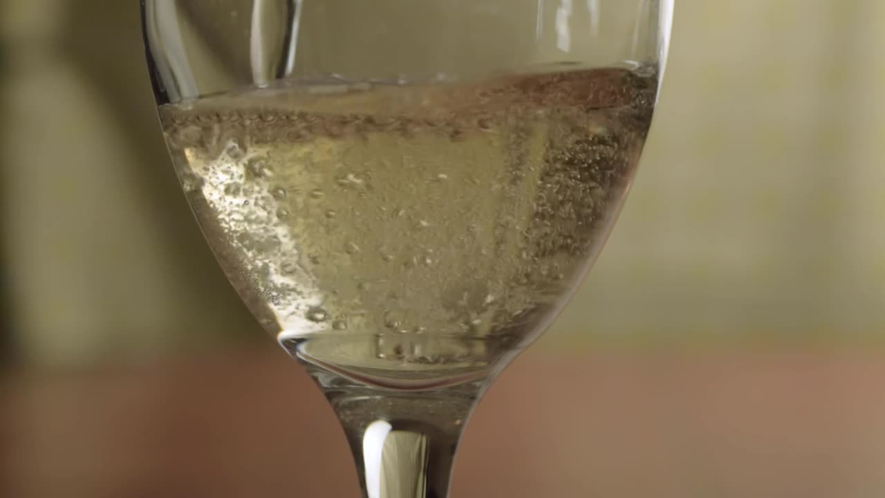 Hand pouring glass of sparkling white wine close up shot