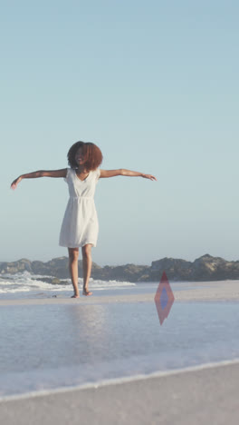 animation of stars over african american woman raising hands at beach