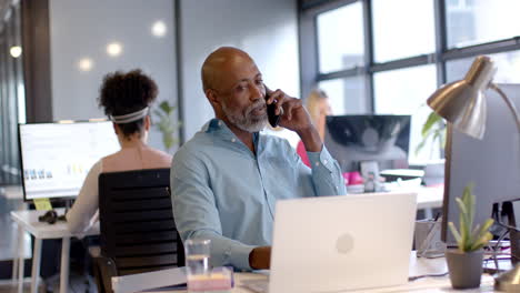 African-american-businessman-using-smartphone-and-laptop-in-office-with-copy-space