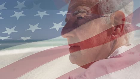animation of senior caucasian man sitting on beach over flag of united states of america