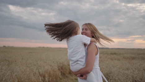 slow motion: young mother holding her daughter in her arms. they are in the middle of the field. mother kisses daughter. mom plays with a little girl in her hands