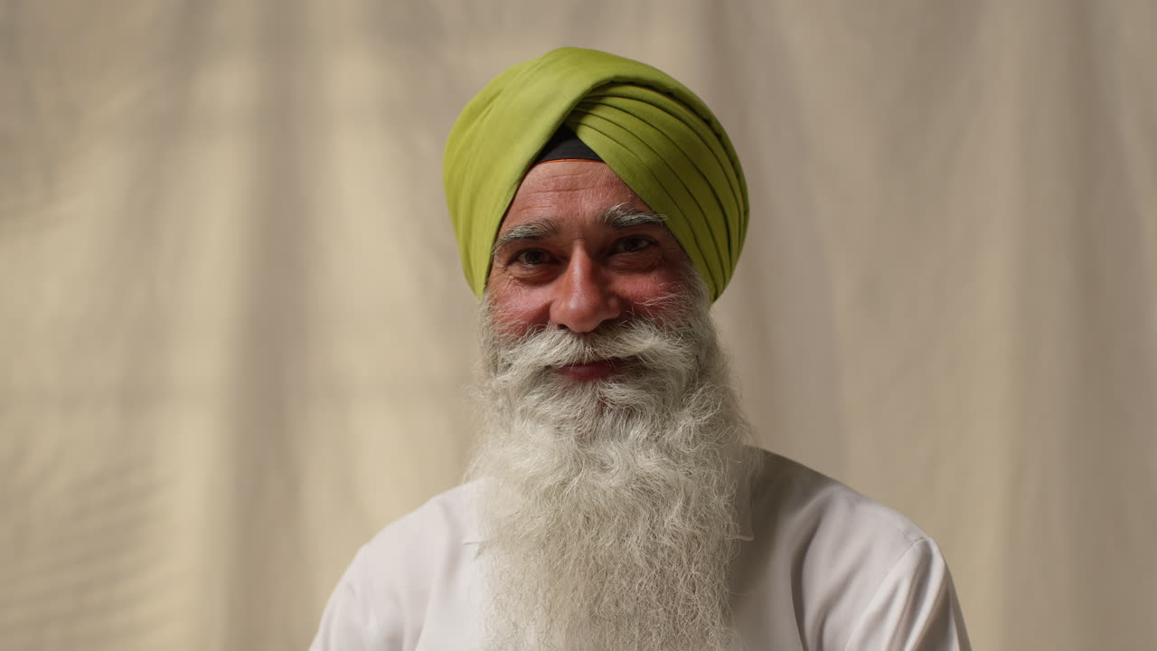 retrato de estudio de un hombre sikh mayor sonriente con barba y turbante contra un fondo plano