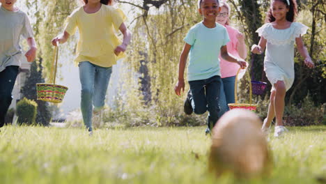 group of children wearing bunny ears running to pick up chocolate egg on easter egg hunt in garden