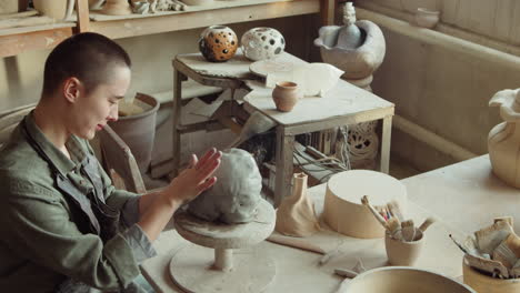 woman sculpting face on clay head in art studio