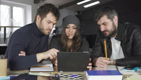 team of young professionals having a meeting in a creative office. looking at the screen of a tablet. business discussion. coffee cups on the table. shot in 4k