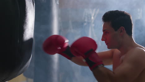 young male boxer hitting punching bag in gym