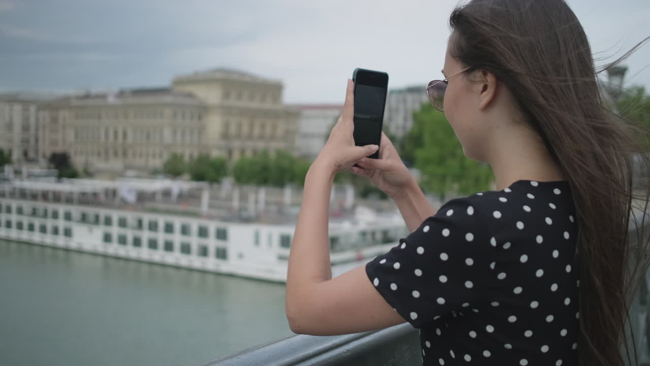 mujer tomando una foto del paisaje de la ciudad desde el puente