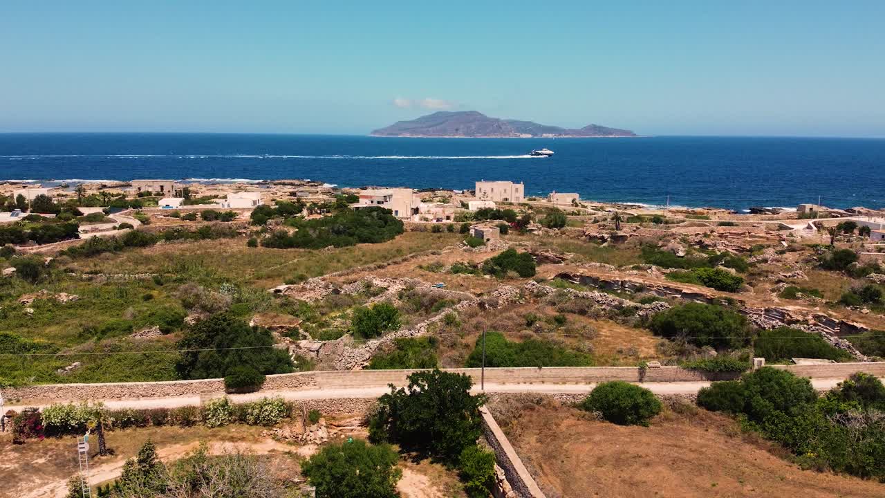 Droneoptagelse der følger en speedbåd, der krydser Middelhavet ud for Favignana, Egadi-øerne, Sicilien. Gamle ruiner og kystlinje i forgrunden, øen Levanzo i horisonten.