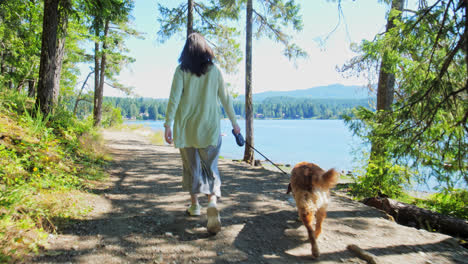 woman walking with golden retriever dog along waterfront park trail, british columbia canada