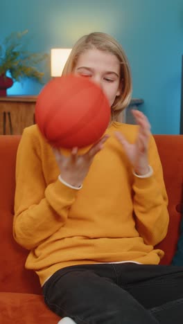 teenager boy on home sofa actively enjoying playing with basketball bouncing ball trying to catch it